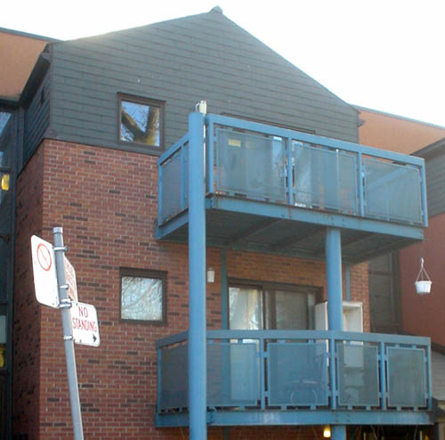 Upper two storeys of gabled brown brick building have blue grated balconies