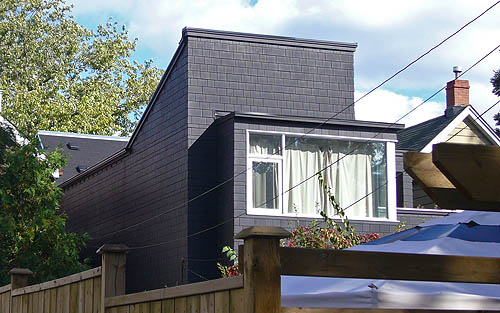 Behind a glass-windowed solarium, roof rises at an abrupt, almost-45° angle