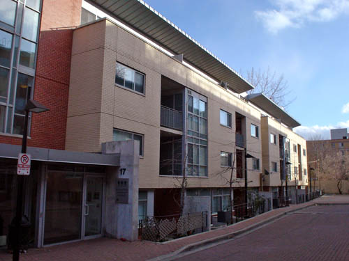 Entrance tower uses dark-red brick and has a concrete retaining wall labeled 17. Buff brick is topped by an aluminum awning over the top floor, with the façade of the building divided into two almost identical modules