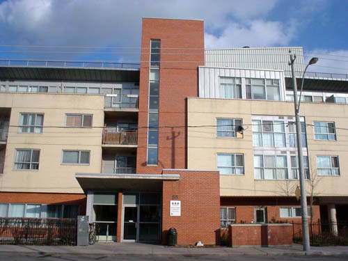 Building has central entrance tower (with offset front wall) in dark-red brick and housing wings on either side in buff brick. Upper storeys are recessed and finished in aluminum