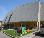 Three north-facing windowless roofs, each set back from the other. Children’s play sets sit on trapezoidal lawn area